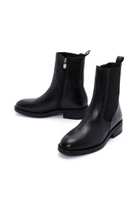 Bottines en cuir noir avec zip sur le côté, panneaux élastiques et semelles plates ; texture lisse avec un design minimaliste et talon renforcé.