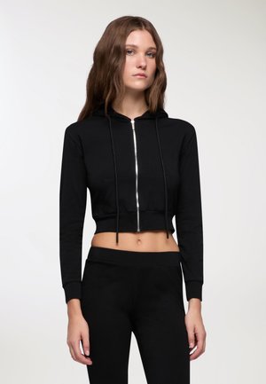 Felpa nera corta con zip integrale e lacci, dotata di una tasca frontale e maniche aderenti, realizzata in tessuto morbido e elastico.
