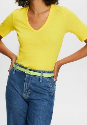 Gelbes, tailliertes V-Ausschnitt-Shirt, kombiniert mit blauen Jeans und einem grünen Gürtel. Das Shirt hat kurze Ärmel und eine gerippte Textur.