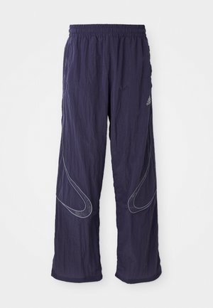 Námornícko modré športové nohavice Adidas s elastickým pásom, širokými nohavicami a reflexnými zakrivenými pruhmi na prednej strane každej nohavice.