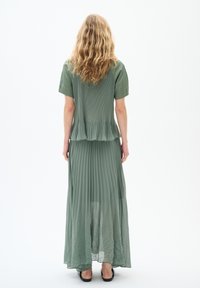 Langes, plissiertes, hellgrünes Kleid mit kurzen Ärmeln und ausgestellt geschnittenem Saum. Weicher, strukturierter Stoff mit einem geschichteten Design und transparenter Überdeckung.
