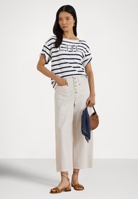 T-shirt de manga curta às riscas em branco e azul-marinho, combinado com calças de perna larga cor bege de cintura alta, com botões decorativos, e um lenço azul-marinho com bolinhas.