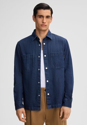Camicia di denim blu scuro con due tasche sul petto, chiusura a bottoni e colletto classico. Maniche lunghe con polsini e orlo dritto.
