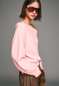 Rosa schulterfreier Pullover aus weichem, strukturiertem Strick; braune hochtaillierte Hose mit fellartigem Akzent; übergroße Schildpatt-Sonnenbrille.