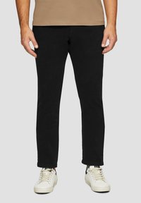 Schwarze Baumwollhosen mit slim fit und leichtem Stretch. Kombiniert mit weißen Sneakern, die ein sauberes, minimalistisches Design zeigen.
