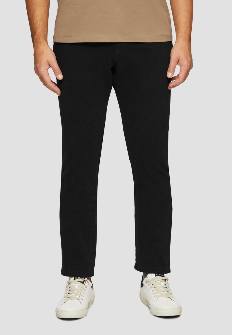 Schwarze Baumwollhosen mit slim fit und leichtem Stretch. Kombiniert mit weißen Sneakern, die ein sauberes, minimalistisches Design zeigen.