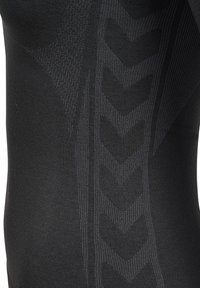 Zwarte basislaag top van een gestructureerde stof, met een subtiele chevronpatroon en ribgebreide accenten aan de zijkant voor extra detail.