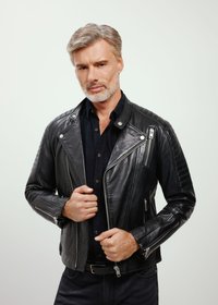 Czarna skórzana kurtka motocyklowa z pikowanymi akcentami na ramionach, licznymi zamkami błyskawicznymi i dopasowanym krojem. Stylizowana na ciemnej koszuli.