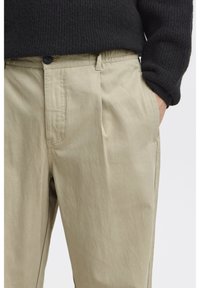 Pantalon chino beige à coupe droite, avec poches avant, passants pour ceinture et fermeture par bouton. Tissu doux avec une texture lisse.