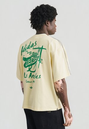 T-shirt jaune oversize avec un motif graphique vert au dos portant le texte "Adidas Los Angeles". Manches courtes, col rond côtelé.