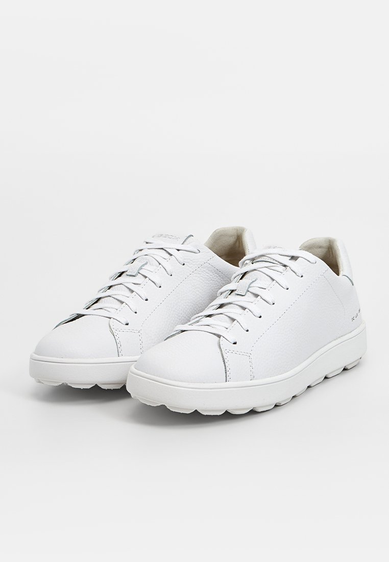 Une paire de baskets basses en cuir blanc avec des lacets et des semelles texturées, présentée sur un fond blanc.