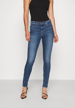 Jeans ajustados en denim azul oscuro, con un diseño clásico de cinco bolsillos, ligero desgastado y una silueta ajustada. Combinados con una blusa negra.