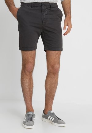 Męskie ciemnoszare bawełniane szorty z podwiniętym dołem i standardowymi przednimi kieszeniami, zestawione z szarymi zamszowymi sneakersami z białymi paskami.