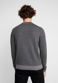 Grå tröja med ett texturerat stickat mönster, rund halsringning, ribbade muddar och fåll. Har en subtil ton-i-ton kontrast i stickdesignen.