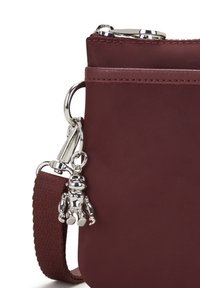 Bolso bandolera burdeos con correa de tela texturizada y llavero en forma de robot de metal plateado unido cerca de la cremallera.