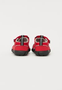 Czerwone buty na zewnątrz z miękkiego materiału, czarne gumowe podeszwy, regulowane paski i wyściełane wnętrze. Posiadają przeszywane akcenty i uchwyty z tyłu.