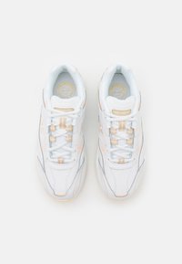 Paire de chaussures de course blanches New Balance avec des accents beige clair, lacées, vues de dessus sur un fond blanc uni.
