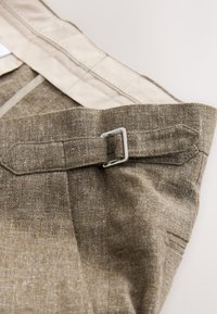 Brunt tekstureret stof med et subtilt mønster, med en sølvfarvet metalspænde på bæltesløjfen og en cremefarvet inderfor.