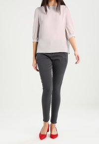 Blusa rosa chiara con maniche a sbuffo, abbinata a jeans skinny grigi scuri e tacchi a punta rossi. Colori semplici e design elegante.