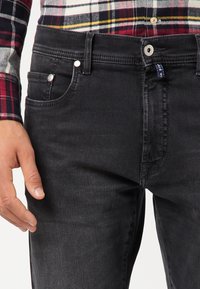 Jeans in denim nero con una vestibilità slim, design a cinque tasche e chiusura con bottone, caratterizzati da cuciture sottili e una superficie texture.