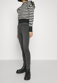 Suéter a rayas en blanco y negro con hombros abullonados, combinado con jeans ajustados en gris oscuro y botas de tobillo gruesas negras.