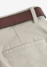 Los pantalones de algodón beige presentan una textura suave, una cinturilla de imitación de cuero marrón y un bolsillo trasero único con delicados detalles de costura.