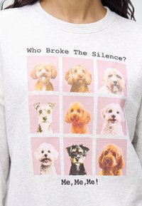 Суичър с девет портрета на кучешки глави в мрежа с текста "Who Broke The Silence? Me, Me, Me!" на светъл фон.