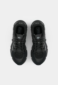 Baskets de sport noires avec une tige en maille texturée, des accents lisses, des lacets ronds et une semelle épaisse et rembourrée. Logo Lacoste sur la languette.