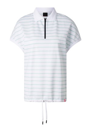 Kobieta ubrana w białą koszulkę polo z krótkim rękawem w jasnoniebieskie paski, jasnoszarą spódnicę za kolano z kieszeniami na suwak oraz masywne beżowe sneakersy.