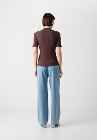 Braun gerippter Kurzarmoberteil, kombiniert mit hellblauen weit geschnittenen Jeans. Das Oberteil hat einen abgerundeten Halsausschnitt und die Jeans sind locker geschnitten.