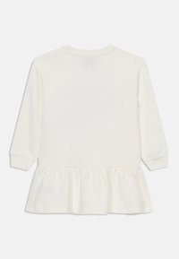 Haut à manches longues crème avec un col rond et un ourlet à volants froncés. Tissu en coton doux ; design simple sans motifs ni accents supplémentaires.