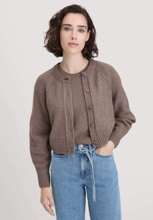 Donkerbruine gebreide cardigan met een ronde halslijn, knopen sluiting en geribde manchetten. Gepaarde met lichtblauwe hoogGESNEEDE spijkerbroek.