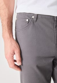 Pantalones de algodón grises con una textura suave, que cuentan con botones metálicos blancos, detalles en los bolsillos frontales y una vista cercana de una mano reposando sobre la tela.