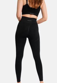 Schwarze, hoch taillierte Leggings aus dehnbarem Material, mit glatter Textur und einem Logo-Akzent am Bund.