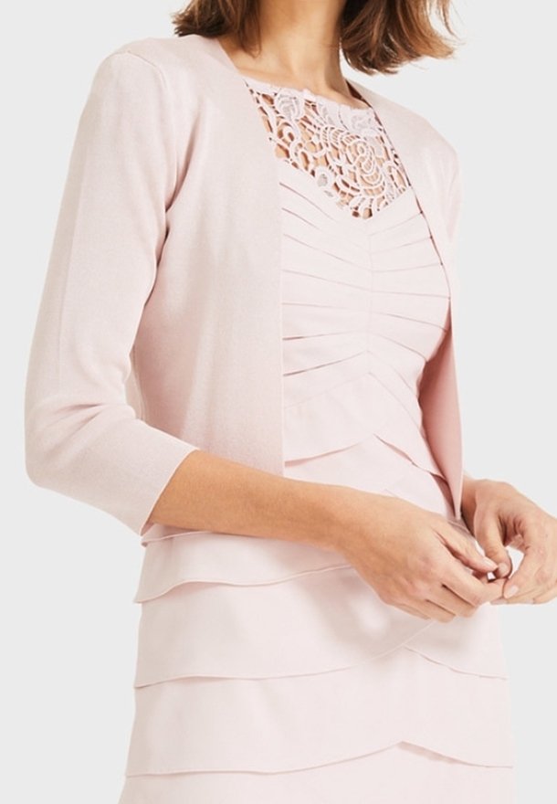 Femme portant une robe rose pâle à couches avec un col en dentelle fleurie et un cardigan assorti à manches trois-quarts.