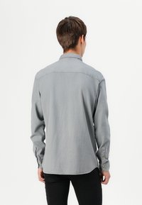Camisa gris de manga larga con cuello con solapa y puños con botones. Hecha de tela suave con una textura sutil y con un dobladillo recto.