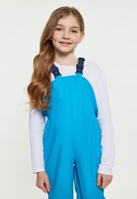 Mėlynos vandeniui atsparios kombinezonai su reguliuojamomis tamsiai mėlynomis petnešomis, derinami su baltais ilgomis rankovėmis marškiniais. Lygi tekstūra, praktiškas dizainas lauko dėvėjimui.