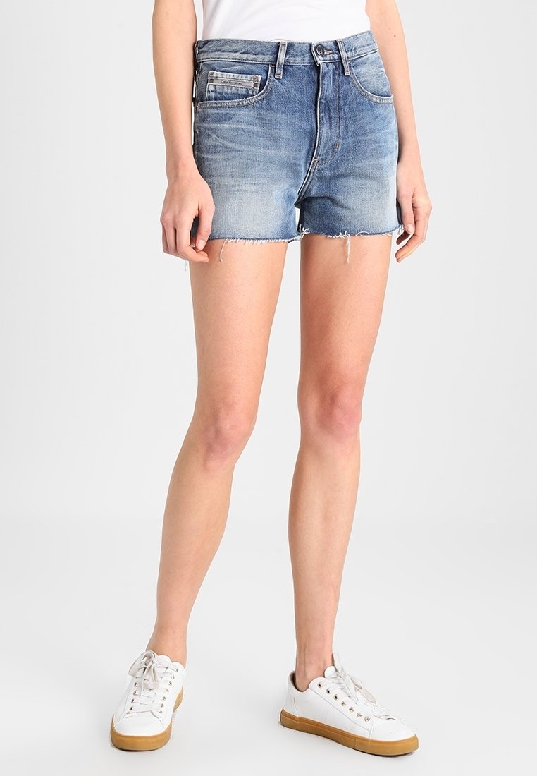 Pantalones cortos de mezclilla con un dobladillo deshilachado, lavado azul claro, cinco bolsillos y un corte clásico. Combinados con zapatillas blancas y una camiseta sencilla.