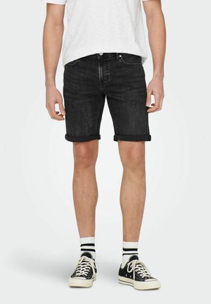 Sorte denim shorts med opfoldede buksekanter, med et klassisk fem-lomme design. Kombineret med en hvid skjorte og sorte sneakers.