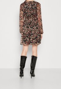 Musta kukkamekko pitkillä hihoilla ja kootulla vyötäröllä. Puolisin läpinäkyvä kangas, jossa on pieniä värikkäitä kukkakuvioita. Yhdistetty polveen ulottuviin mustiin saappaisiin.