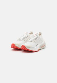 Witte sportieve schoenen met een gestructureerde bovenkant, reflecterende accenten en een roze loopvlak. Voorzien van veters en een trekband bij de hiel.