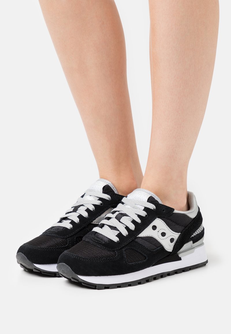 Zwarte en grijze sneakers met suede en mesh materiaal, witte veters en middenzool, met een onderscheidend zijlogo en gestructureerde details.