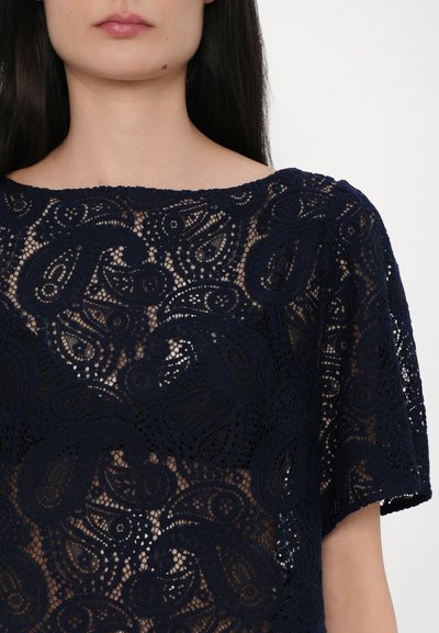 Navy blue lace top featuring intricate paisley patterns, short sleeves, and a wide neckline, with a sheer texture throughout.