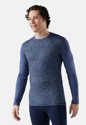 Marineblauwe langemouwen shirt met een gestructureerd geometrisch patroon op de voorkant, effen mouwen en een ronde halslijn; ontworpen voor comfort en mobiliteit.