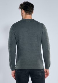 Dunkelgrau gestrickter Pullover mit Rippstruktur, Rundhalsausschnitt und dezenten horizontalen Mustern entlang der Ärmel. Figurbetonter Stil, schlichtes Design.