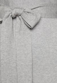 Tissu gris côtelé avec un détail en nœud noué à la taille. Le matériau semble doux et texturé avec une finition lisse.