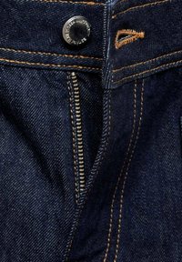 Jean en denim bleu foncé avec une fermeture éclair métallique partiellement déverrouillée et un bouton en métal, présentant des coutures contrastantes orange.