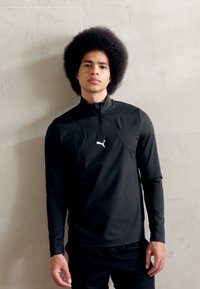 Juoda ilgomis rankovėmis sportinė marškinėliai su užtrauktuku, pasižymintys prigludusia forma ir mažomis baltomis logotipu ant krūtinės, pagaminti iš lygaus audinio.