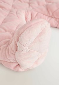 Couverture en peluche rose avec un motif matelassé, présentant une texture douce et moelleuse avec un bord arrondi. Brillance notable de la surface du tissu.