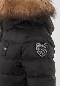 Czarna kurtka puchowa z odpinanym kapturem obszytym futrem, srebrną naszywką z logo z rhinestonami na ramieniu oraz pikowaną teksturą.